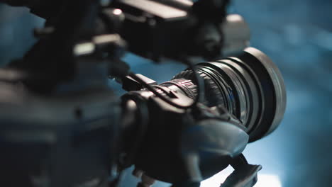 close up camera lens on professional video rig reflecting neon studio lights, revealing focus ring textures and optical glass elements, showcasing precision mechanism for broadcast filming