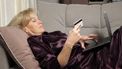 una mujer de mediana edad paga sus compras en línea a través de una computadora portátil