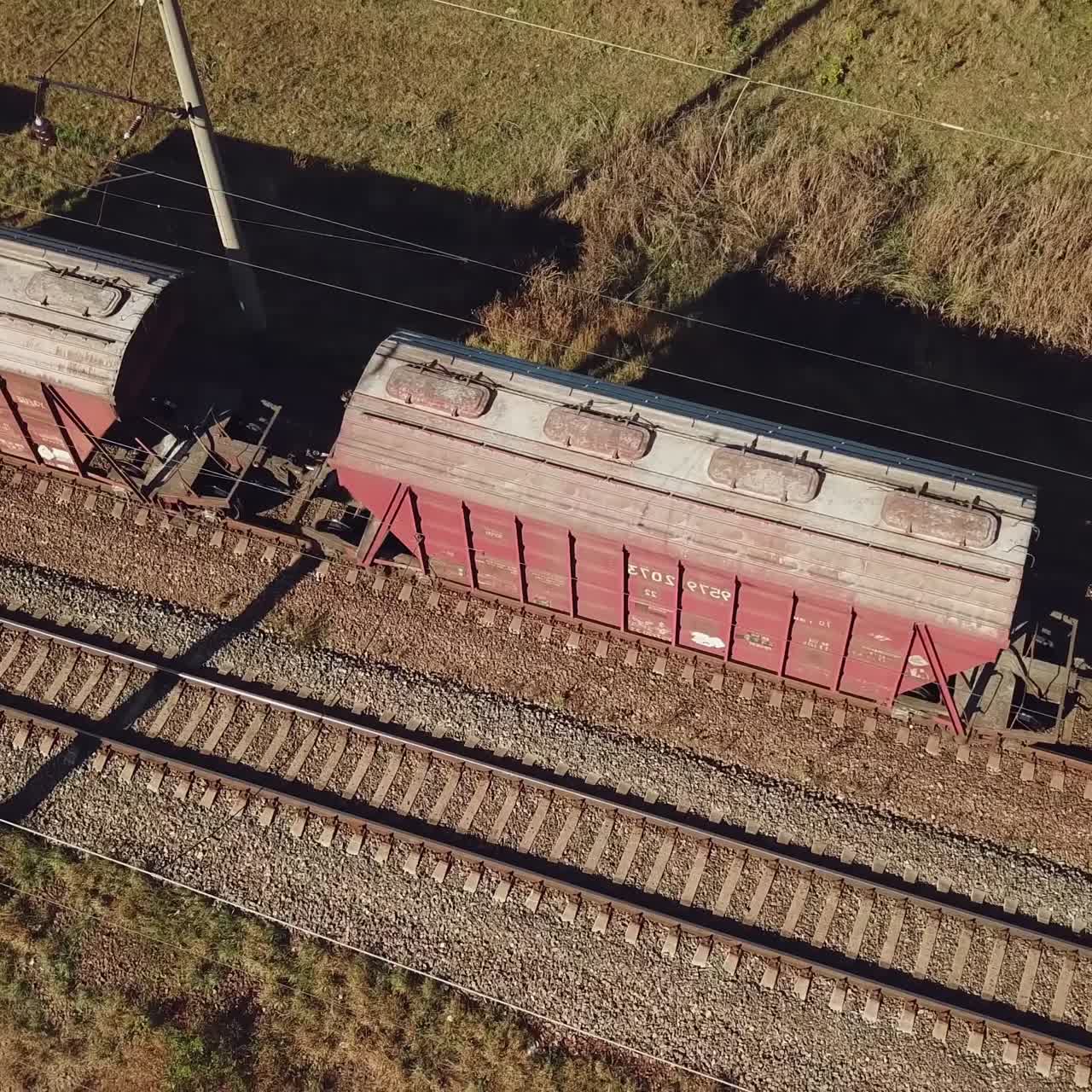 freight train with wagons is passing by rail near landings with trees on the background of fields in warm weather. Aerial view