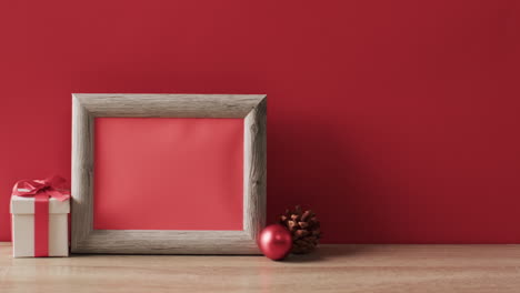 video of christmas decorations and wooden frame with copy space on red background