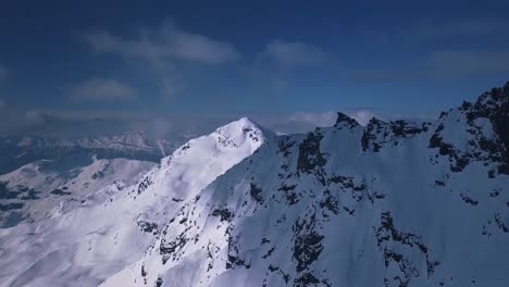 Aerial-drone-shot-flying-over-tall-snow-covered-mountain-range-above-the-vacation-resort-town-of-Verbier,-Switzerland