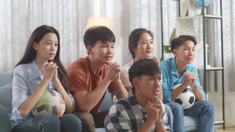 asian teenagers cheering and watching football game on tv and celebrating victory at home