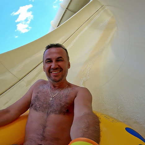 happy man on yellow inflatable ring in water slides. man goes down from water slide to swimming pool in aqua park. slow motion.