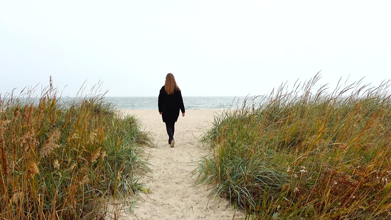 Pigen går på stranden ved havet på en sti.