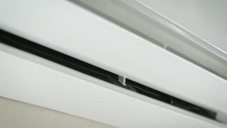 white air conditioner is turning on with swing function and blowing cold air in bright room