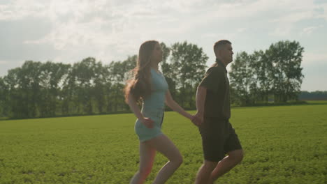 side view of couple running through green field, woman long hair swaying in breeze as she gasps for breath tiredly, man powering stride ahead
