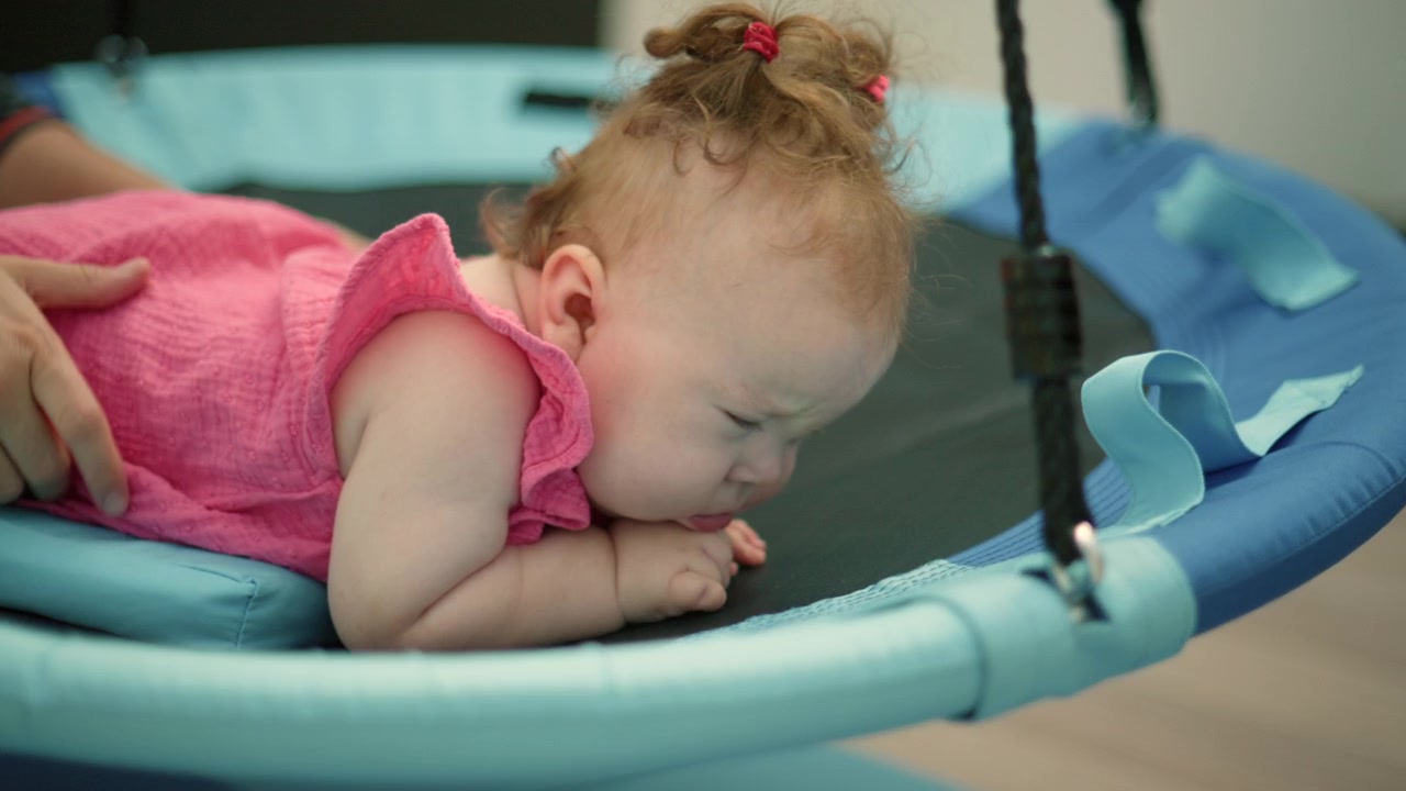 Physiotherapist positioning baby with Down syndrome on a therapy swing. Infant receiving developmental support and early intervention