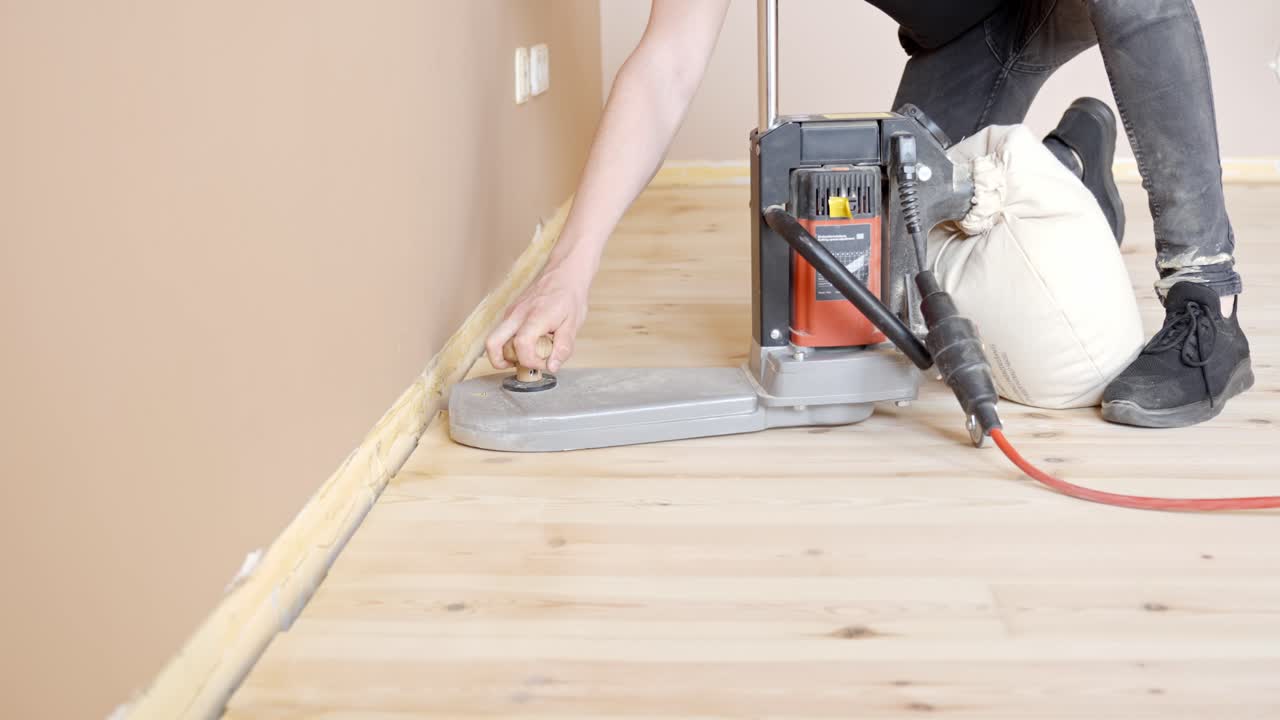 Power sander used along baseboard to finish wood flooring edges in empty room, skilled tradesperson