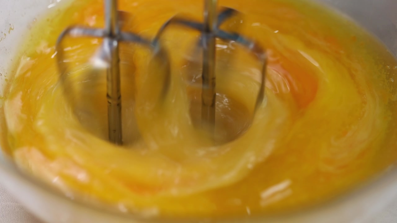 Close up of electric mixer whisking raw eggs in bowl during baking preparation in kitchen