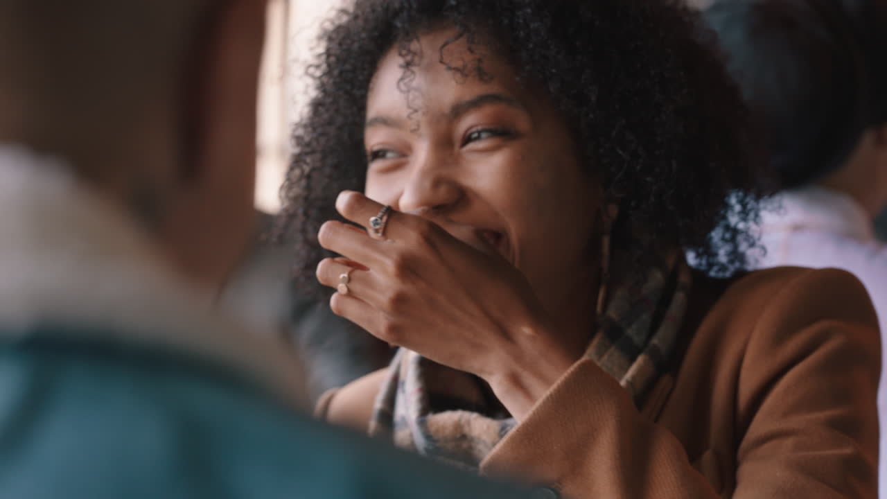 happy african american woman chatting with friend in cafe laughing enjoying gossip conversation hanging out in busy restaurant for lunch meet up