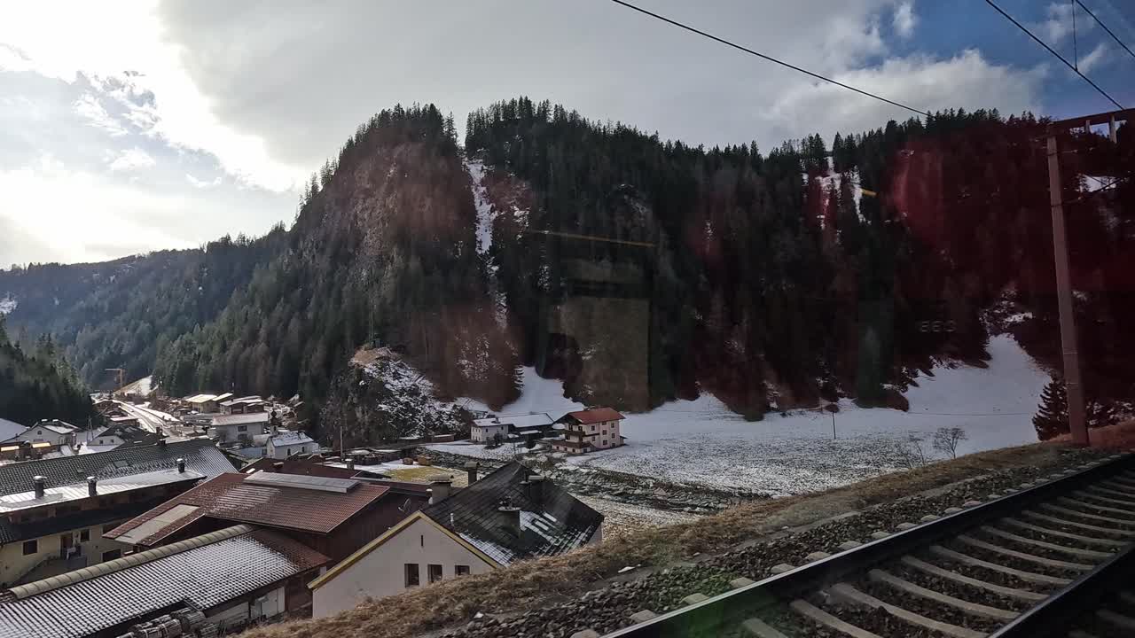 Snowy alpine village nestled in the mountains seen from train window in the Alps during winter