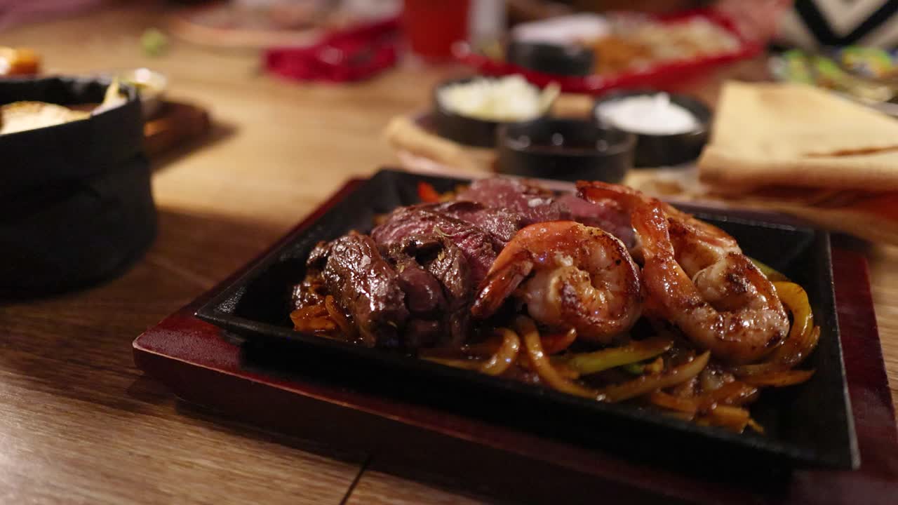 Close-up of sizzling beef fajitas on a wooden table in a vibrant restaurant setting with warm lighting