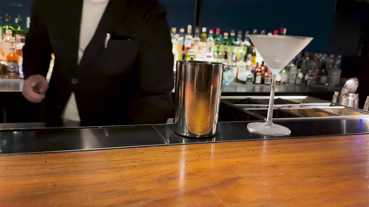 A professional bartender in a suit prepares a drink behind a wooden bar counter