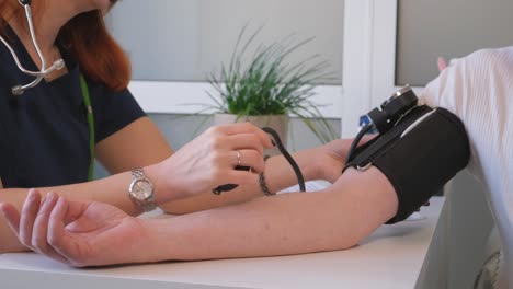medical professional wearing purple gloves checks male patient blood pressure with sphygmomanometer beside stethoscope. doctor focuses on doing work