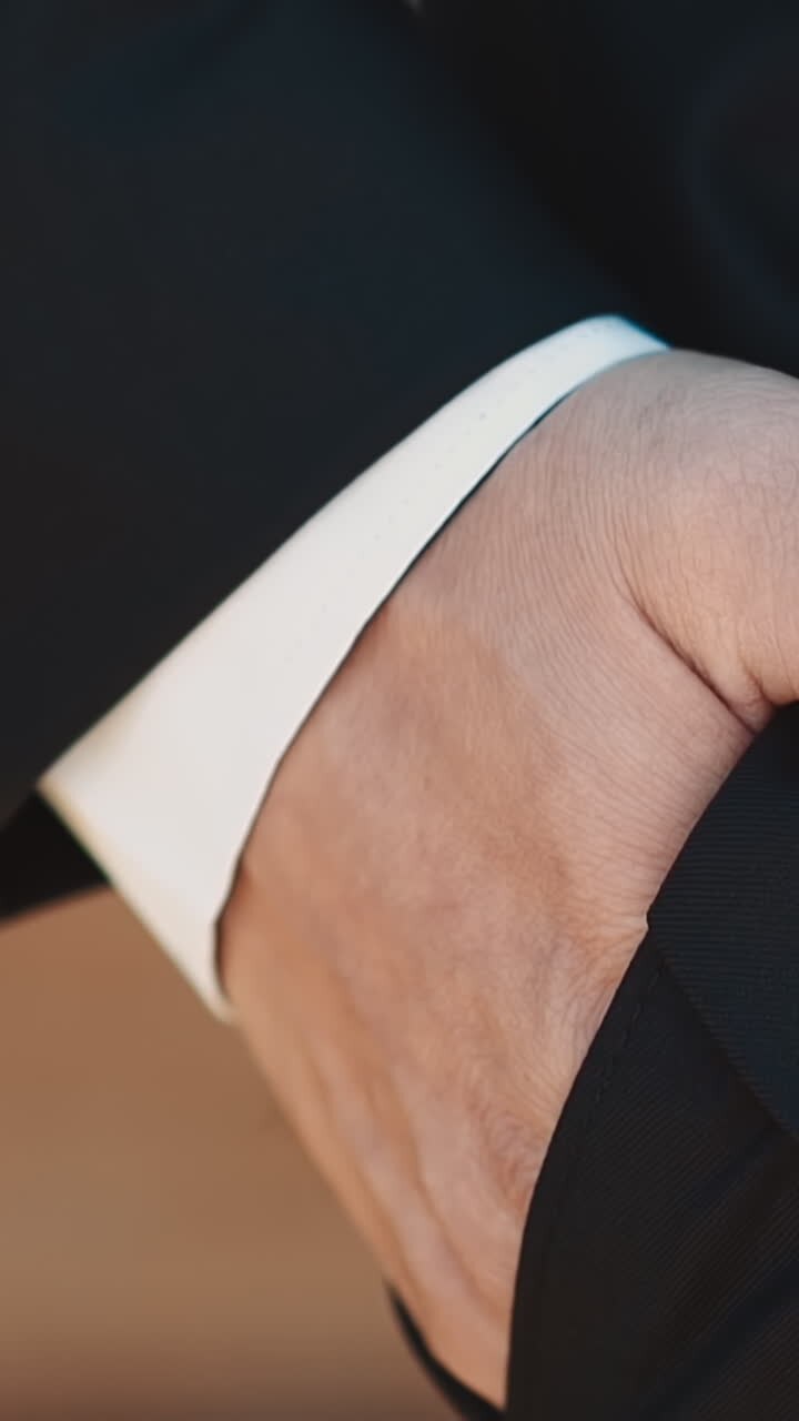 Man with gold wedding ring puts hand into pocket of suit trousers on blurred background closeup slow motion. Just married guy at wedding ceremony