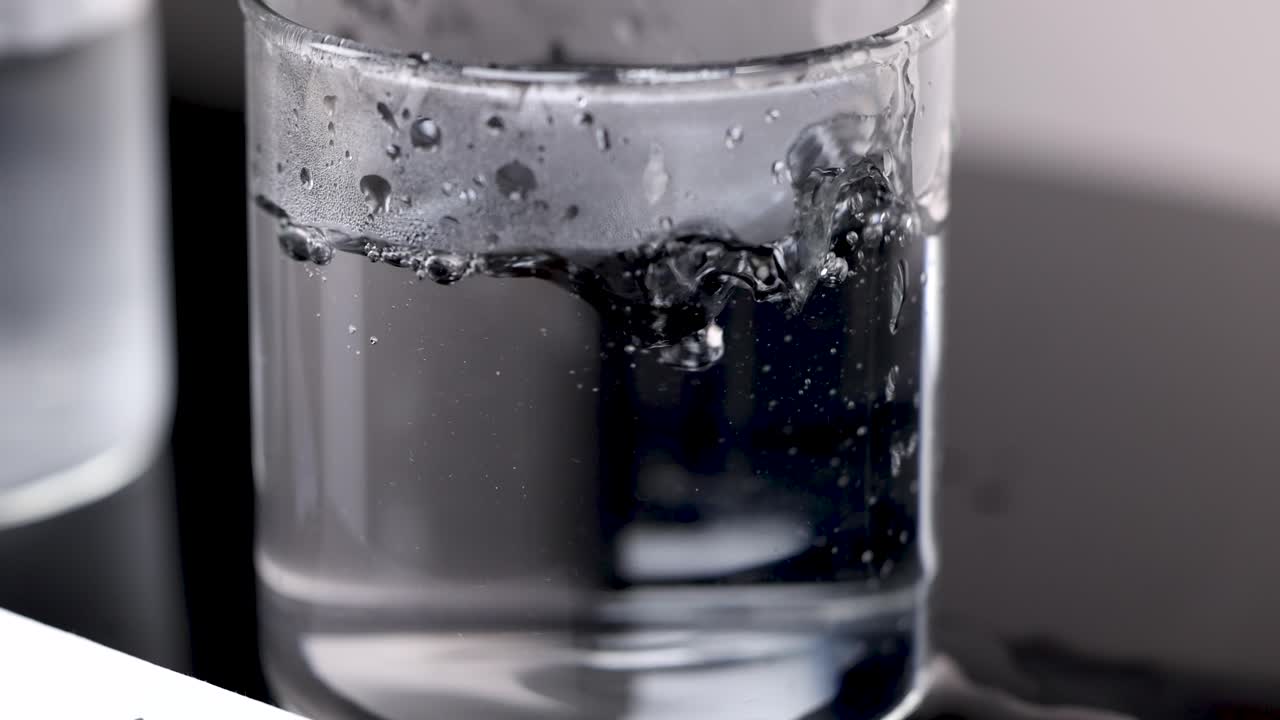 Ice cube rapidly melts and bubbles in clear glass of hot water, high-speed macro shot