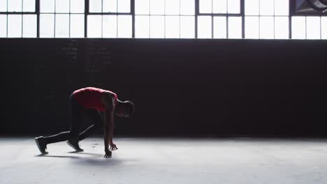 african american man kneeling starting a run in an empty building