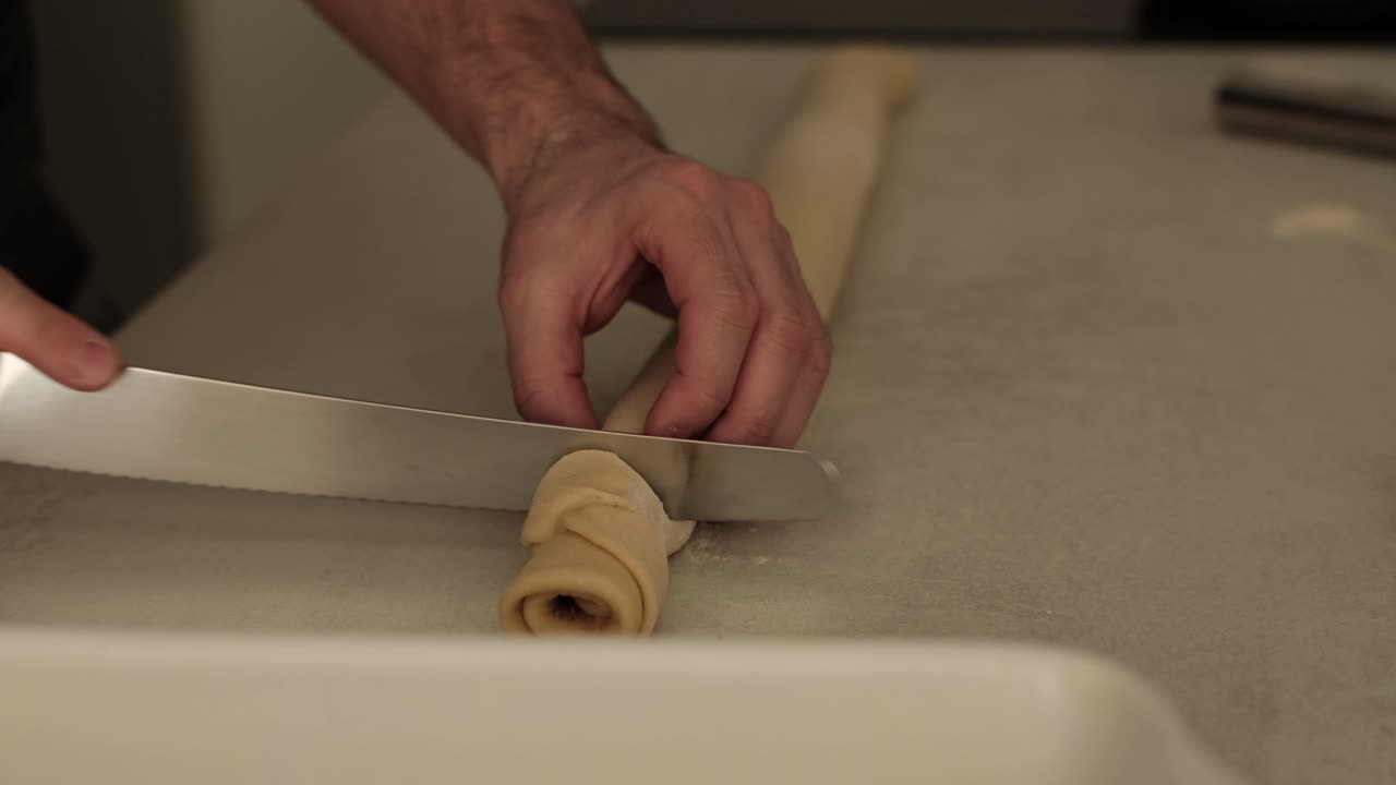 cocinero blanco masculino comenzando a cortar rollos de canela hechos en casa en la encimera de la cocina