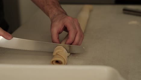 cocinero blanco masculino comenzando a cortar rollos de canela hechos en casa en la encimera de la cocina