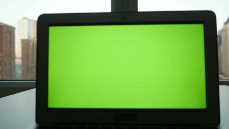 computadora con pantalla verde en un edificio de oficinas moderno con fondo de paisaje urbano.