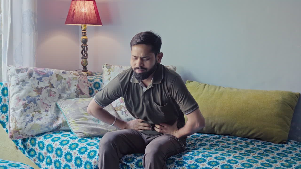 Asian man having stomachache while sitting on a sofa at home.