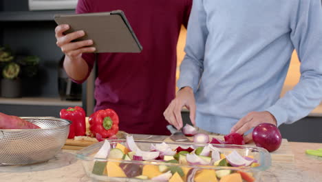 preparing vegetables, multiracial gay couple using tablet for cooking in modern kitchen, at home
