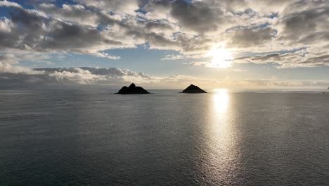 Silhouetten-Luftdrohnen-Seitenschwenk-Der-Mokulua-Inseln-Bei-Sonnenaufgang,-Der-Den-Gesamten-Horizont-Und-Die-Wunderschöne-Sonne-Zeigt,-Die-Aus-Den-Wolken-In-Lanikai-Hawaii-Hervorragt