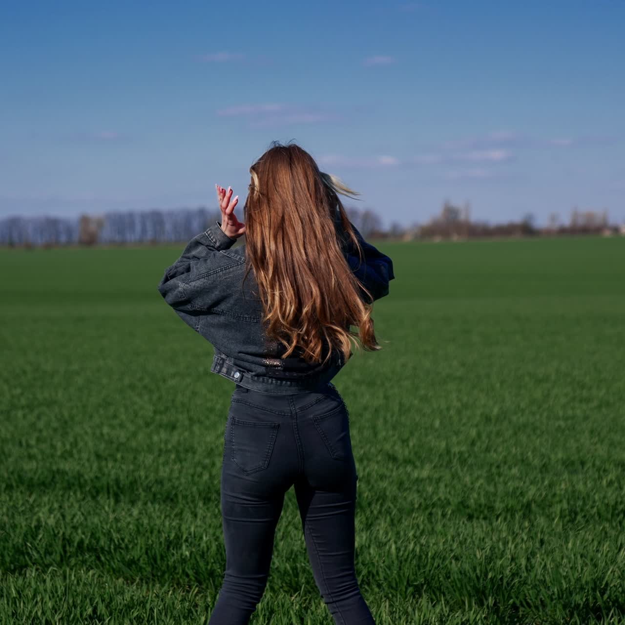 Attractive young woman walking on green field. Beautiful model with long fluttering hair on green nature background. Slow motion
