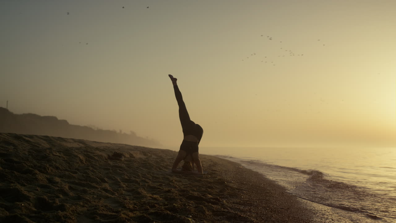 머리에 서서 스트레칭하는 실루 ⁇  소녀. 해가 뜨면 요가 훈련하는 여성.