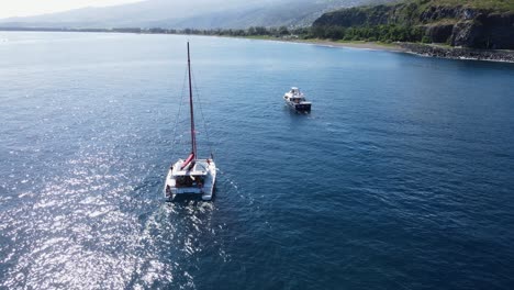 drone footage of a catamaran with people and another boat near a cliff at the reunion island