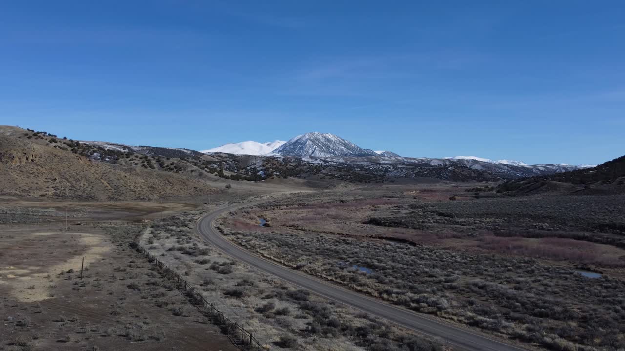 Drone shot of a snow-covered mountain towering over the hills and valley below in Northern Nevada. The mountain is contrasted by the highway and the river, tying together this wild rural landscape.