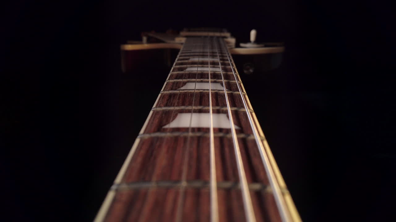 Slow tracking shot up the fretboard of a Gibson Les Paul electric guitar with the camera moving towards the guitar body