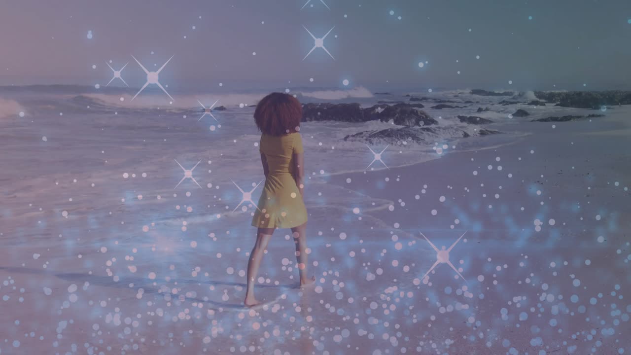 Donna che cammina a piedi nudi sulla riva, entrando tra le onde, impronte, scintillio ai piedi che evoca il viaggio.