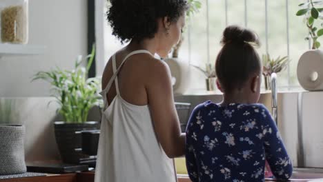 Happy-african-american-mother-and-daughter-washing-dishes-in-kitchen,-slow-motion,-unaltered