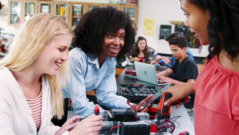 high school teacher with female pupils building robotic vehicle in science lesson