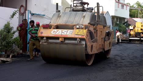 wide shot of workers skillfully operates a road paving machine to construct a new road in tamil nadu, india. the machine lays asphalt precisely while workers patch any holes.
