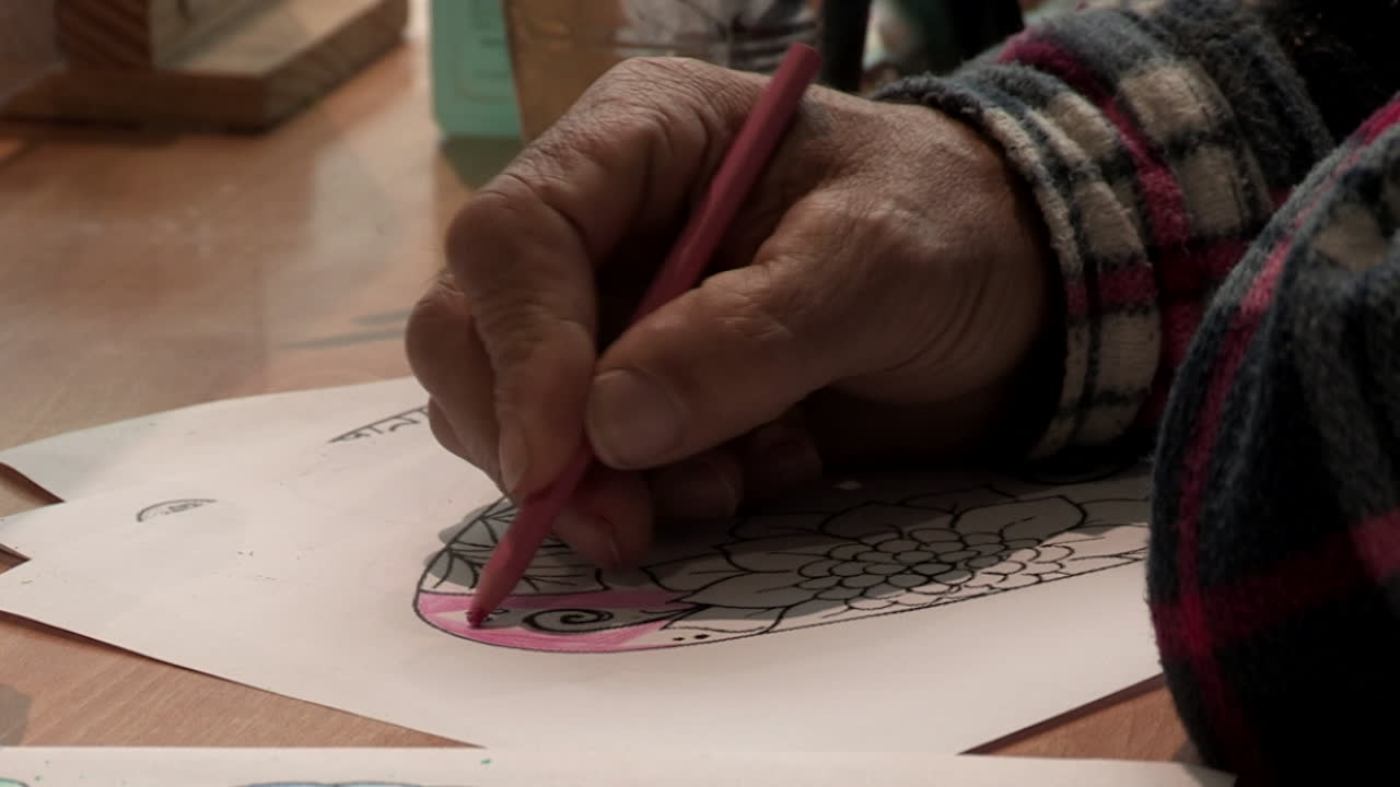 primer plano de la mano de un hombre, pintando un dibujo, con lápiz rosa