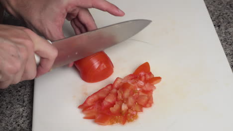 man chopping fresh tomato into pieces on the board