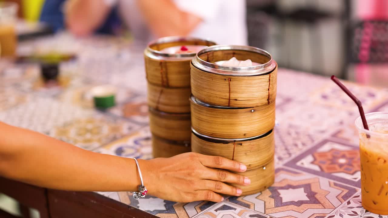 Hands serve bamboo steamers filled with dim sum on a patterned table in a vibrant Phuket setting