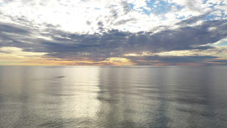 aerial: locked shot of baltic sea during golden hour with majestic horizon with orange and blue colours in the sky