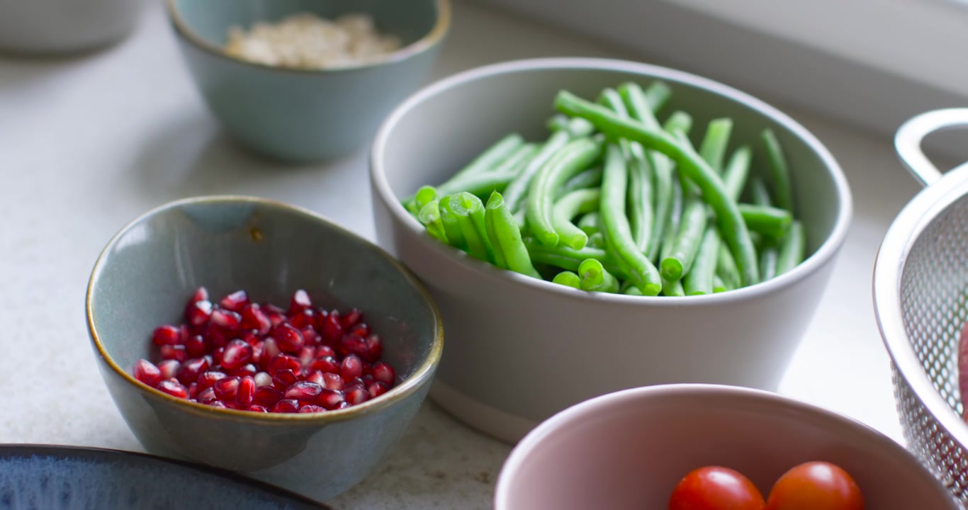 Camera is shifting frame around bowls on countertop, pulling focus to center green beans and arils