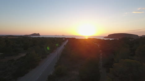 Drone-shot-of-a-road-cutting-through-trees-to-the-coast