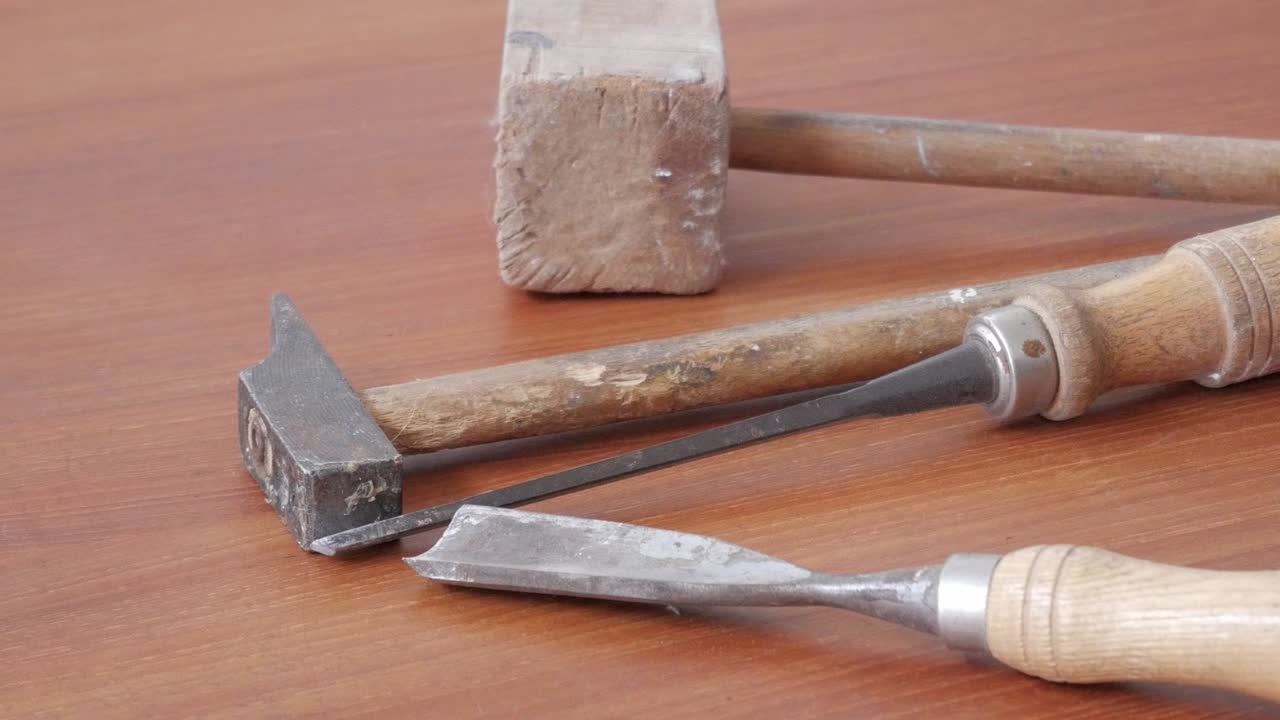 Zoom out showing an antique woodworking hammer and chisel placed on a wooden table