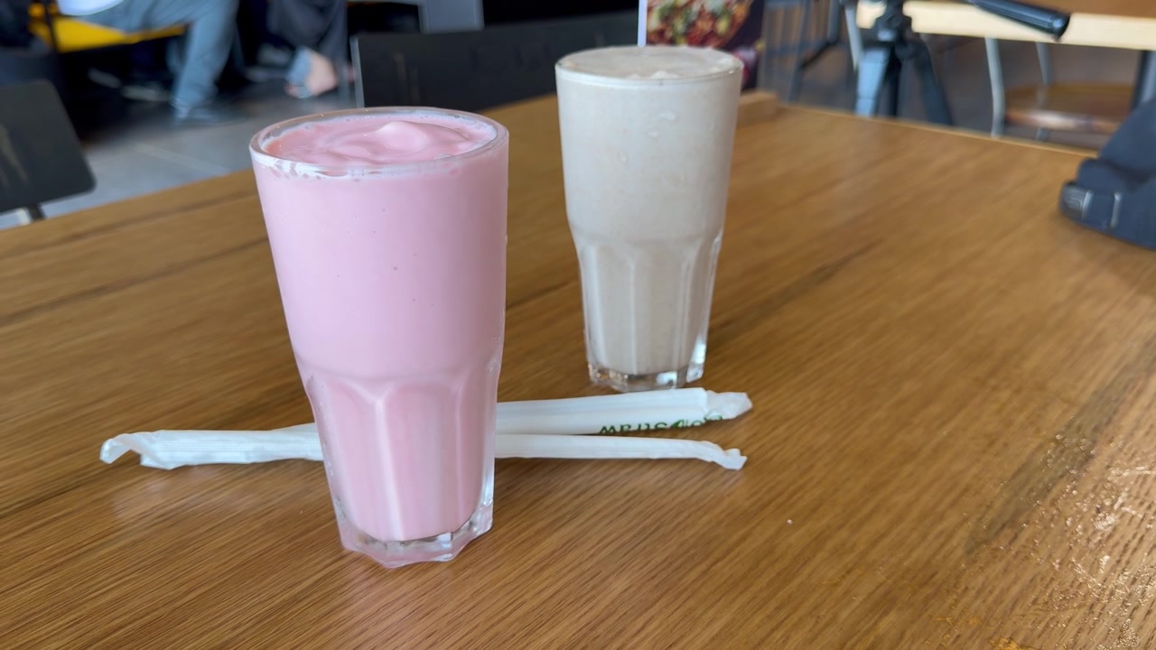 A pair of Shakes on a wooden table in a cafe.