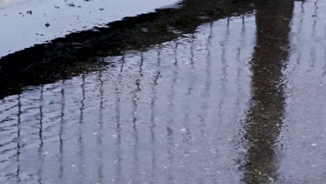 Rain-splashing-in-a-puddle,-with-metal-fence-reflected