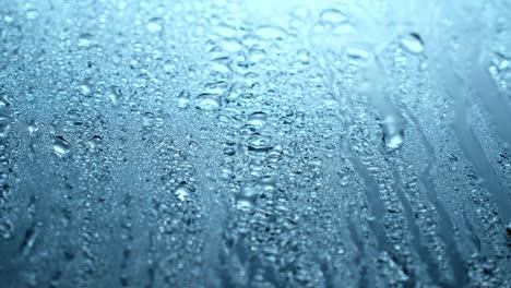 close up view of water drops falling on glass. rain running down on window. rainy season, autumn or spring. raindrops trickle down, dark blue sky. close up, soft focus.