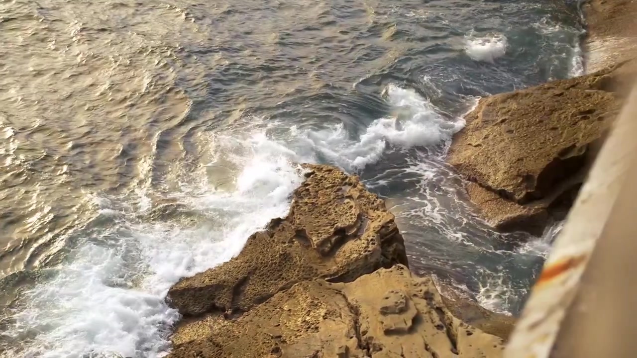Onde che si infrangono contro le rocce su una costa europea al tramonto a San Sebastian, Spagna, ripresa a mano