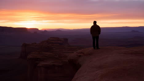 Man Standing on a Cliff Overlooking a Vast Canyon Landscape at Sunset