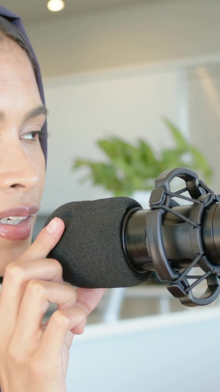 Video verticale: Inizio ripresa, una donna con foulard si china per regolare il microfono in studio, con spazio per il testo.