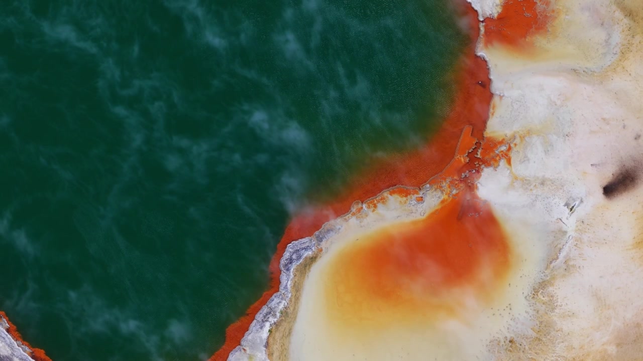 Vista aerea con drone dall'alto della colorata costa geotermica di Rotorua, Isola del Nord della Nuova Zelanda, che evidenzia vivide formazioni minerali arancioni accanto ad acqua termale color smeraldo e motivi astratti naturali.